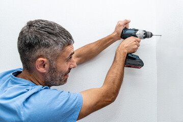 Man repairman makes hole with drill, repair work with construction equipment