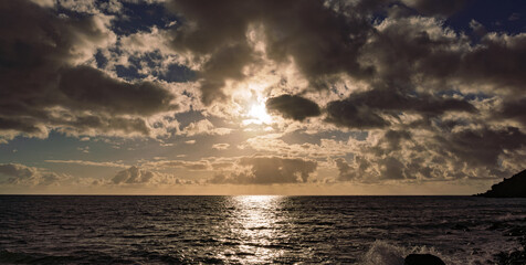 Colorful sunset casting shimmering light over restless ocean with clouds above