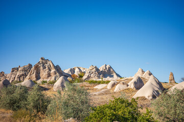 A stunning landscape of Cappadocia, Turkey, featuring its iconic fairy chimneys and smooth rock formations shaped by centuries of natural erosion. Warm sunlight illuminates the beige and sandy texture