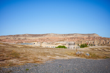 A wide-angle view of Cappadocia&rsquo;s famous desert-like landscape featuring layered plateaus, unique rock formations, and small village structures in the distance