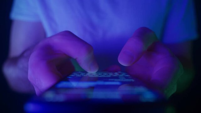 Close-up view of hands typing a message on smartphone illuminated by neon light. Texting, chatting in messenger app, late-night online communication, social media activity, and digital interaction.