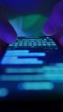 Close-up of fingers typing text message on smartphone keyboard in dark environment. Macro view of chatting on phone. Modern communication, messaging apps and social media. Vertical video