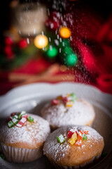 mixed fruit cupcakes dusted with powdered sugar, styled on a festive table for the Christmas and New Year holiday season. The cupcakes are topped with colorful candied fruits and arranged on a rustic 