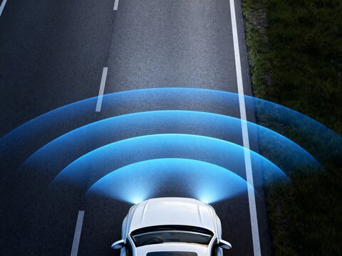 Overhead view of a white car on a road, emitting blue sensor waves; autonomous driving technology, safety systems visualization.
