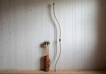 Traditional recurve bow and leather quiver with arrows, natural wood and leather colors, archery and hunting equipment, against a white wooden plank wall