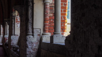 Architectural view of Riga Dome Cathedral&rsquo;s red brick walls and aged stone columns from shaded corridors, revealing medieval textures and sacred atmosphere.