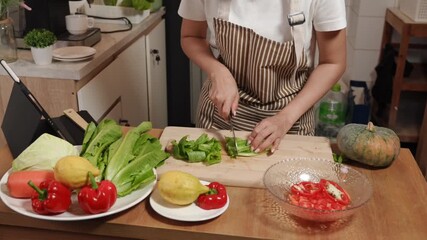 Overhead shot of an Asian woman chopping fresh lettuce on a wooden board, preparing a healthy salad with various vegetables in her kitchen - Powered by Adobe