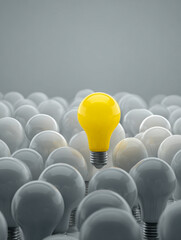 Obraz premium A bright yellow light bulb standing out in a sea of white bulbs symbolizing unique ideas and innovation against a neutral gray background
