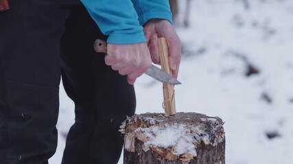 Making feather sticks from pine in winter forest close up with bushcraft knife