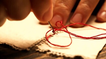 Close-up of hands meticulously sewing fabric with red thread.