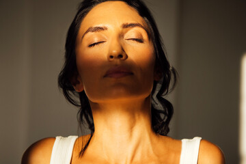 Woman with closed eyes, basking in warm sunlight, showcasing serene expression and natural beauty, highlighting peaceful moment of self-reflection and tranquility in soft light