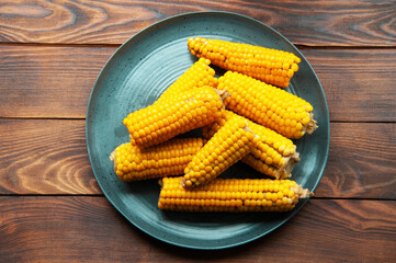 boiled corn in a gray plate on a wooden table. yellow corn in the kitchen on the table
