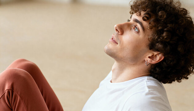 Close-up profile of a thoughtful young man with curly hair looking up. Handsome male model relaxing indoors with a hopeful expression. Contemplation and mental wellness concept with copy space