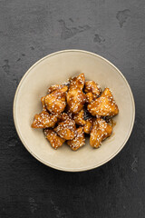 Sesame glazed chicken bites in a bowl on dark stone background
