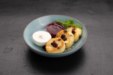 Syrniki pancakes with sour cream and berry jam in a blue bowl, traditional breakfast