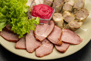 Charcuterie platter with pork slices, sausage, lettuce and red sauce on plate, closeup