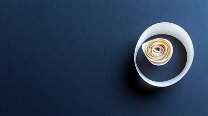 A tightly rolled paper scroll, resembling a spiral or rose, is positioned on a dark blue, textured surface. The lighting creates a subtle shadow, emphasizing th
