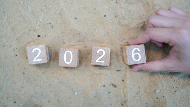 Hand Placing Wooden Blocks Showing Number 2026 on Sandy Background for Concept of Future Year and Progress in Time Management and Planning