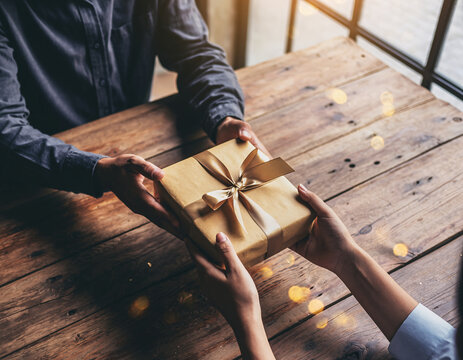 Hands exchanging a golden gift box on a wooden table in warm light