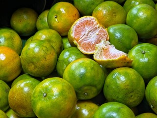 A pile of fresh green and orange tangerines (Shogun/Tangmo oranges), with one fruit peeled open to reveal the pinkish-orange segments.