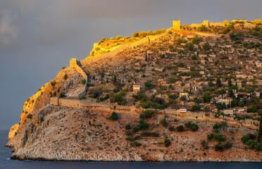 Golden sunset light illuminates Alanya Castle and the ancient fortress walls above the Mediterranean Sea in Alanya Turkey, showcasing historic architecture and scenic coastal beauty