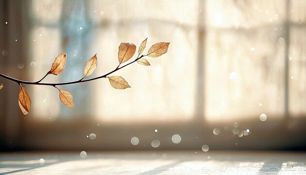 A delicate branch with dry, golden-brown leaves is silhouetted against a softly lit window, with bokeh effects adding a dreamy atmosphere.