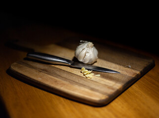 Close-up of a bulb of garlic on a wooden chopping board with a sliced clove of garlic