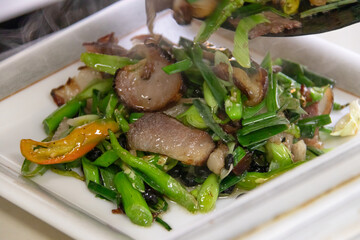 Stir fried pork slices with spring onion, mushroom and chili served on white dish, savory and aromatic