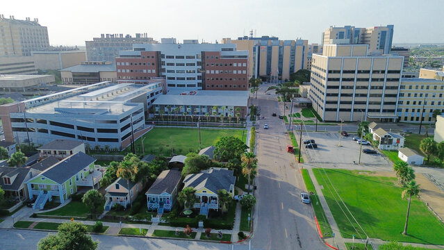 Grassy vacant land near multi-story research, administrative buildings form coastal academic hub, surrounded by green buffers, roadways, port infrastructure visible in distance, Galveston, Texas