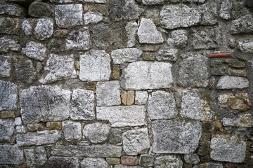 A fragment of a stone wall constructed from stones of various shapes and sizes, held together with mortar. A brutalist gray masonry backdrop