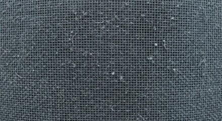 Detailed macro photograph of a dirty metal mesh filter covered in a thick layer of dust, lint, and debris, showing a textured grid pattern and the need for cleaning