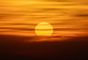 Landscape with large orange sun disk among clouds at sunset