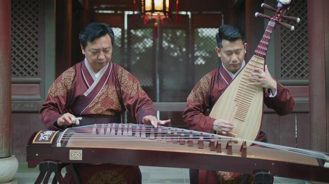 Two mature Chinese men in traditional robes playing classical Chinese instruments, specifically the GuZheng (zither) and the Pipa (lute), outdoors in a traditional Chinese architectural setting