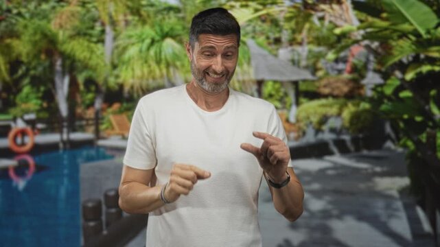 Man smiling and pinching fingers to show small amount while wearing white t shirt at pool resort; playful vacation.