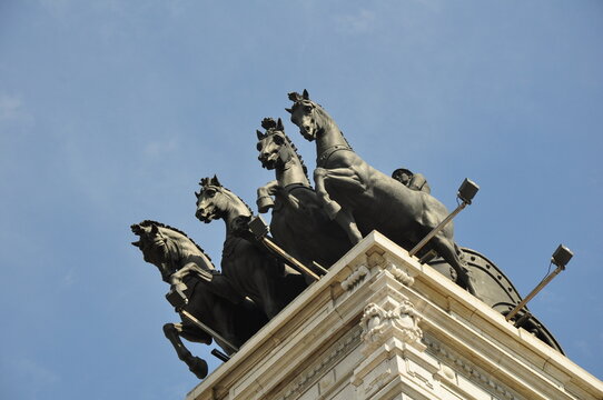 Rooftop quadriga sculpture in Madrid featuring four horses and a charioteer against a blue sky.