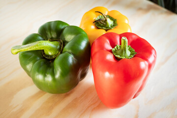 Trio of Vibrant Bell Peppers (Red, Green, Yellow) Grouped on a Light Wooden Surface