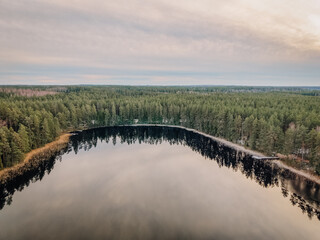 Obraz premium Aerial view of tranquil lake surrounded by lush green forest, reflecting soft clouds and serene atmosphere, showcasing natural beauty and peaceful environment