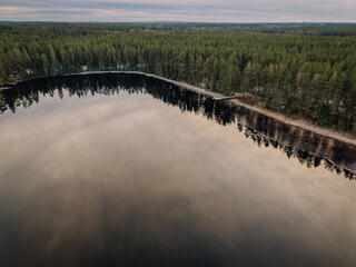 Serene landscape featuring a tranquil lake reflecting surrounding evergreen trees under a cloudy...