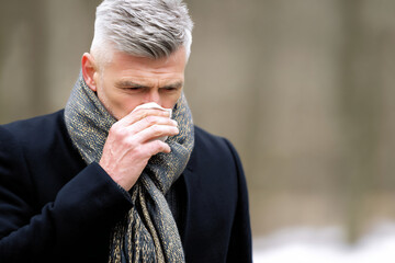 Sick Mature Man Blowing Nose with Tissue Outdoors in Winter Cold