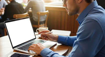 Young man in glasses and blue shirt works on laptop with stylus at cafe table, cup of coffee nearby. Modern freelance, remote work, digital lifestyle, technology and productivity.