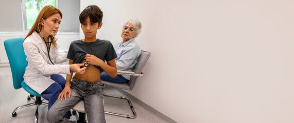 Senior woman looking at physician perform chest auscultation on grandson using stethoscope during...