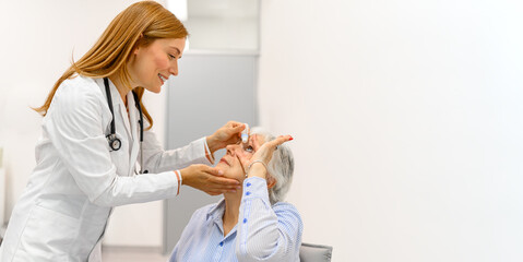 Female doctor putting eye drops in elderly patient's eye during ophthalmology clinic visit for...