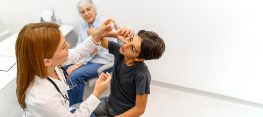 High angle view of senior woman looking at female doctor putting eye drops in boy's eye during routine checkup