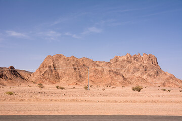 Red rocky desert with a mountain in the background and power lines in the foreground