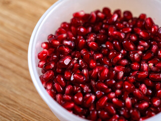 Pomegranate seeds in a plastic bowl on a wooden background. Close up.