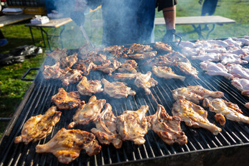 Shallow depth of field (selective focus) details with chicken thighs on a metal barbecue outdoors during a sunny day