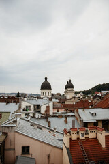 Fototapeta premium An overcast rooftop view of Lviv's historic center, featuring a stately, weathered old church facade with a red tile roof surrounded by light-colored European buildings.