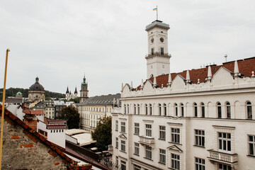 Panoramic view of the historic Lviv Old Town featuring the prominent white Rynok Square clock tower flying the Ukrainian flag, surrounded by classic European architecture.