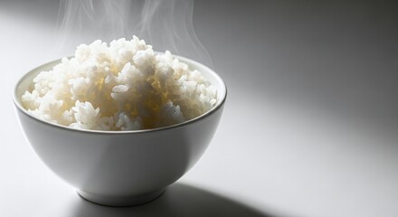 A bowl of freshly steamed white rice is presented, its fluffy grains releasing delicate wisps of steam, set against a clean, bright background, inviting a sense of warmth and nourishment