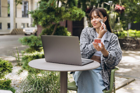 Woman multitasking working on laptop applying makeup outdoors